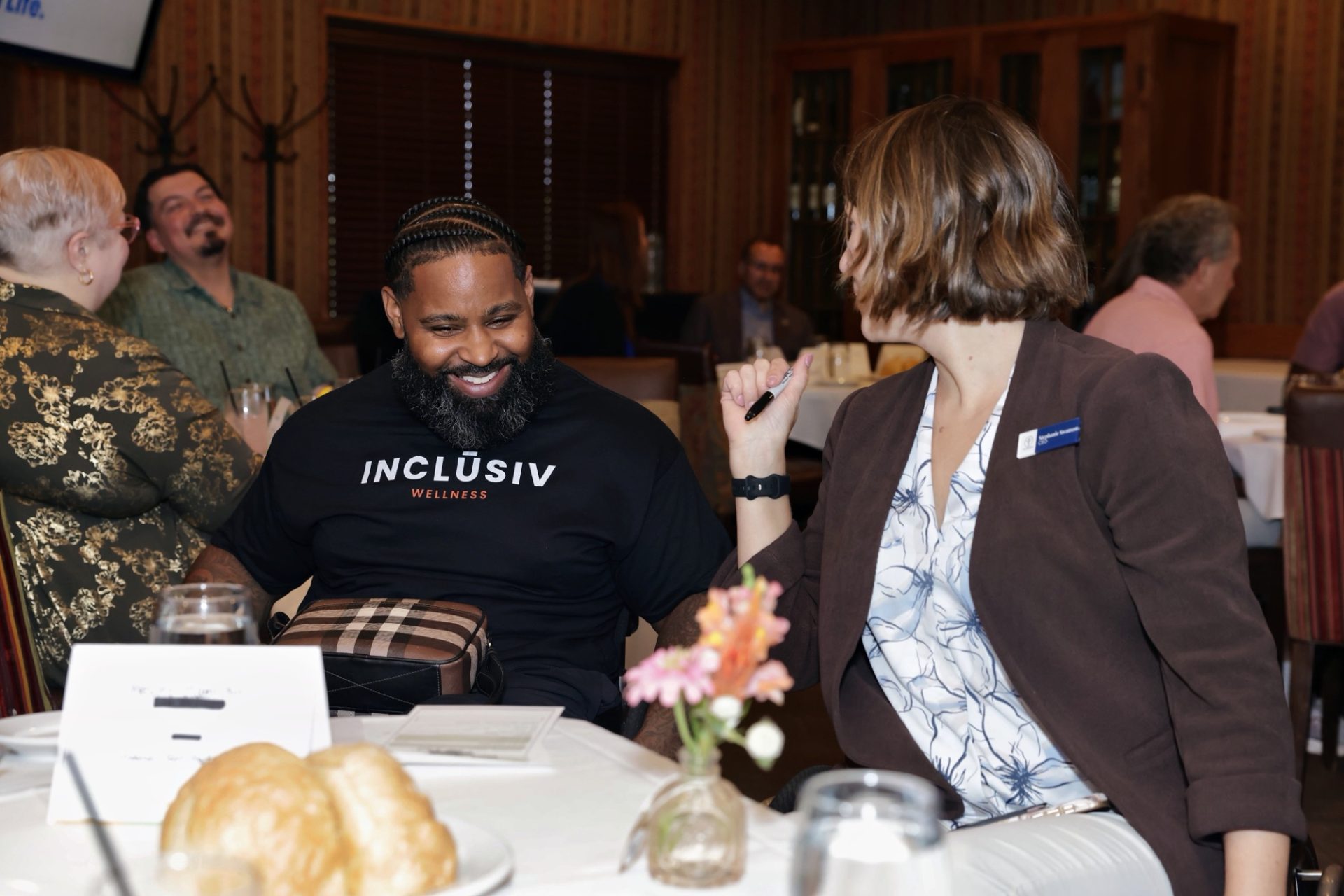 Wesley Hamilton, wearing an INCLŪSIV Wellness shirt, laughing with a colleague at a business luncheon
