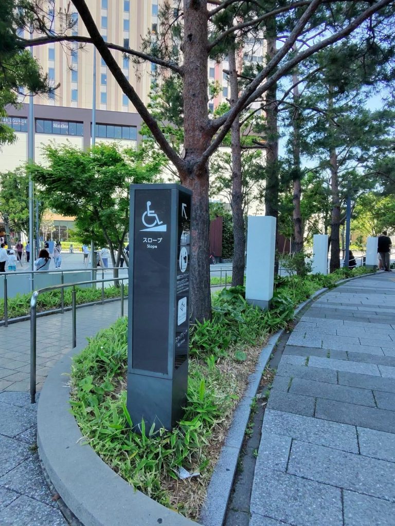 Beyond Barriers travel: a wheelchair-accessible slope sign in Japanese and English beside a ramped city walkway in Asia